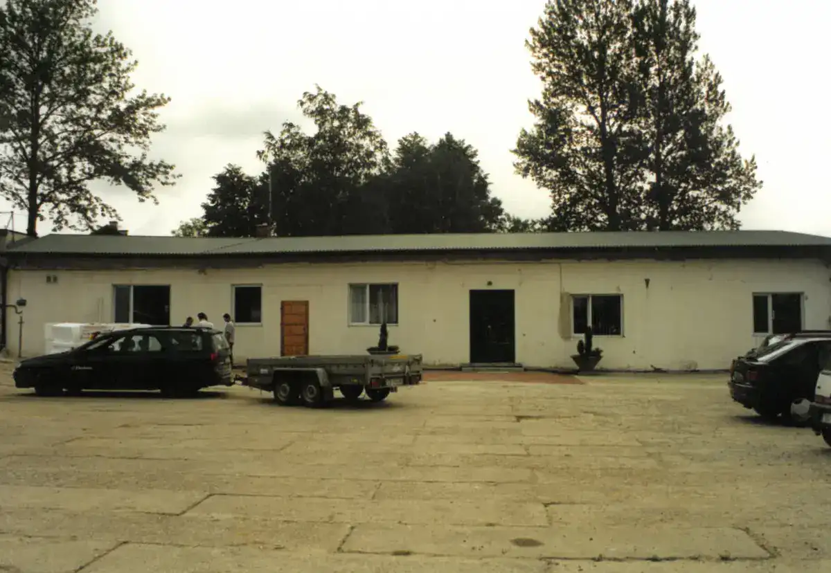 Dawna siedziba hurtowni budowlanej EKOBau – parterowy budynek z białą elewacją, samochodami i przyczepą na placu.