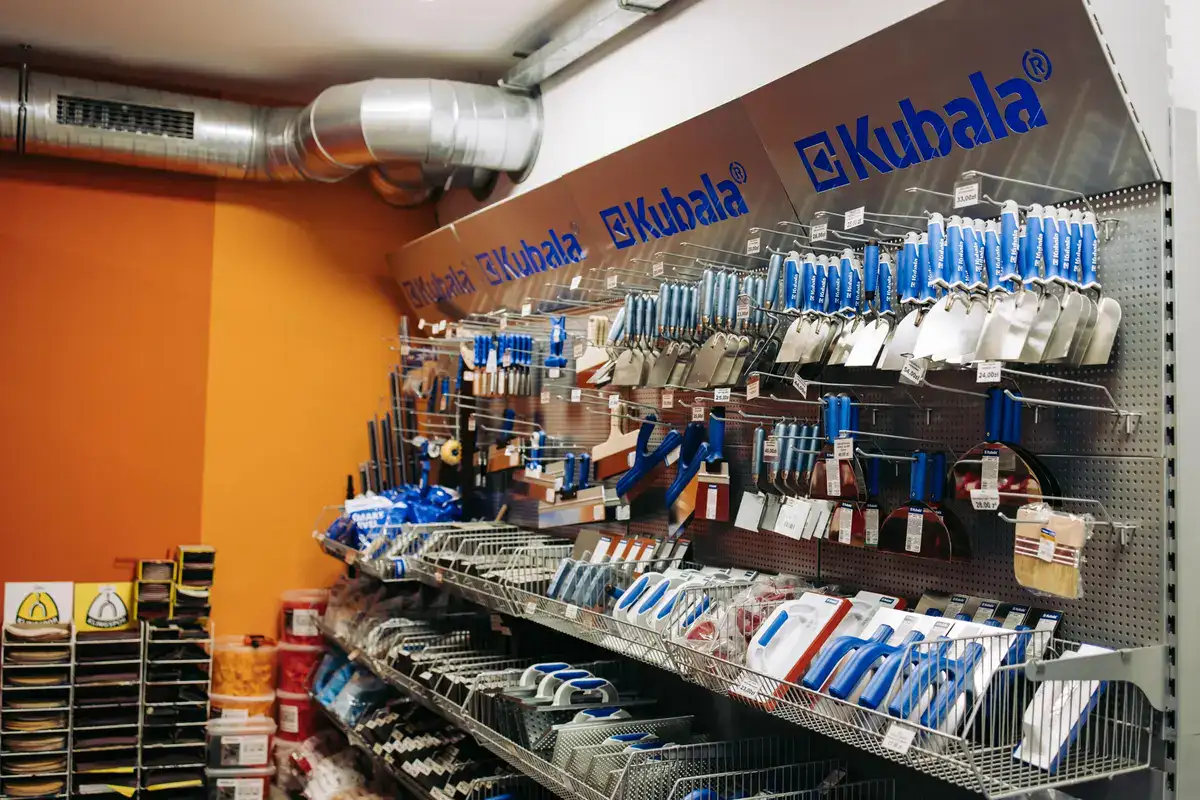 Ściana z narzędziami Kubala w hurtowni EKOBau – szpachelki, pacy, kielnie i akcesoria budowlane na pomarańczowym tle.