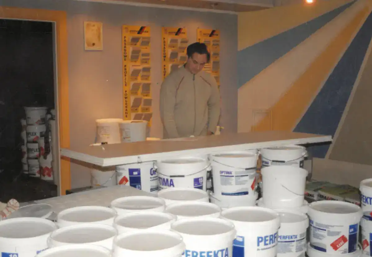 Wnętrze sklepu z farbami – pracownik EKOBau przy ladzie otoczony wiadrami z produktami malarskimi.