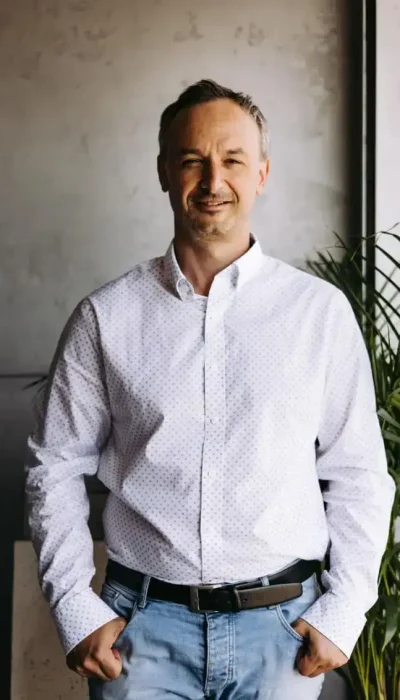 Mężczyzna w białej koszuli stojący w biurze EKOBau, uśmiechnięty, symbolizujący nowoczesne podejście firmy do branży budowlanej.